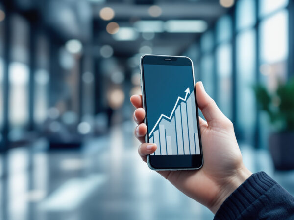 Main &eacute;l&eacute;gante tenant un smartphone affichant un graphique financier ascendant